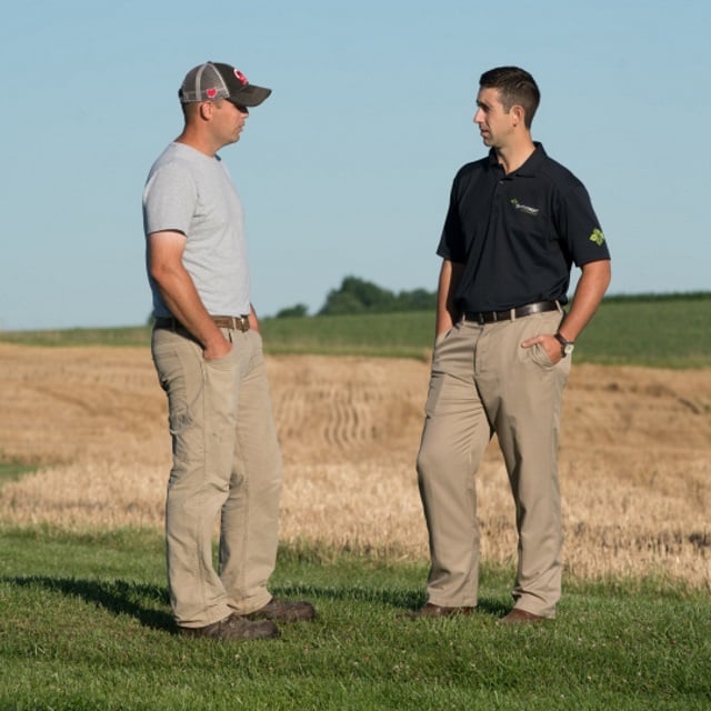 Two men talk in front of a harvested field.